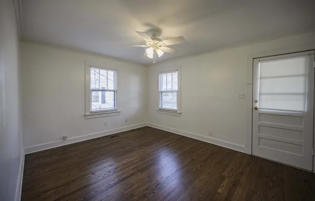 an empty room with wooden floor closet fan and windows