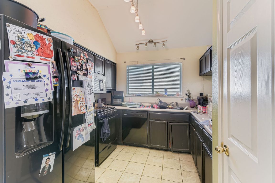 4705 Fallenash Drive Austin, TX 78725 - Photo 4 of 11 Kitchen featuring black appliances, light tile patterned floors, light countertops, vaulted ceiling, and rail lighting