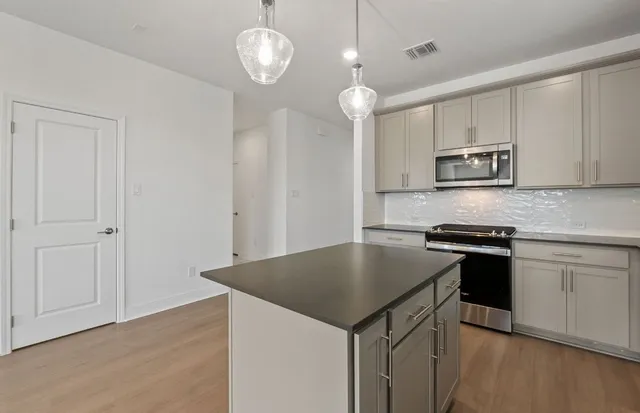 a kitchen with stainless steel appliances granite countertop a sink a stove a refrigerator and island with wooden floor