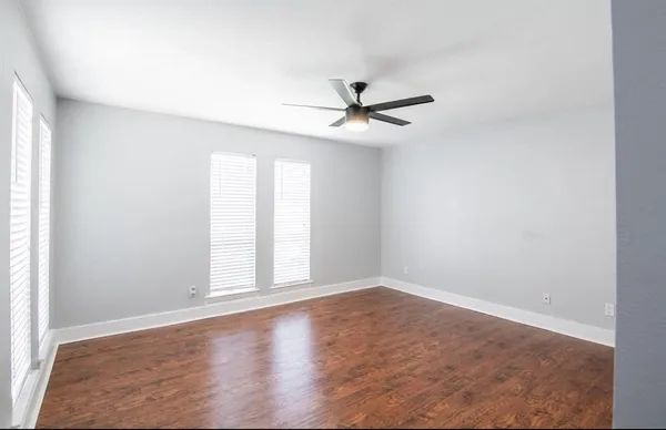 an empty room with wooden floor fan and windows