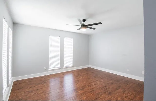 an empty room with wooden floor fan and windows