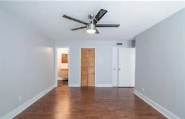 a view of an empty room with wooden floor and a ceiling fan