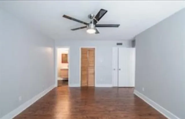 a view of an empty room with wooden floor and a ceiling fan