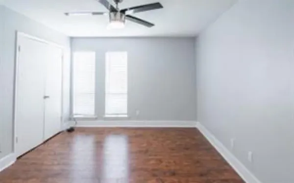 an empty room with wooden floor fan and windows