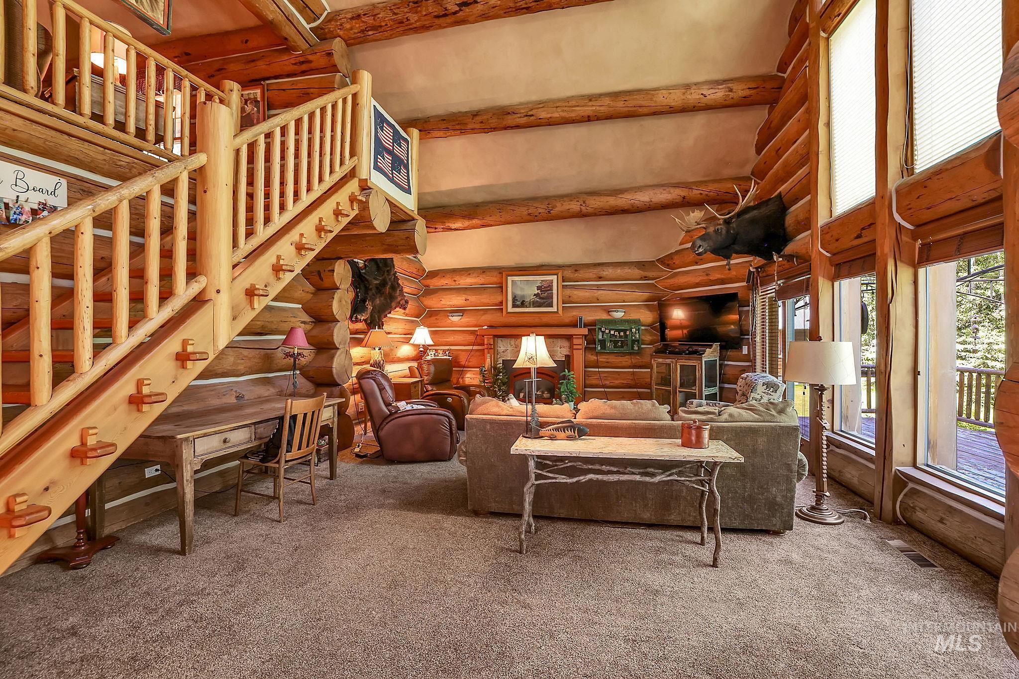 1345 Divot Lane McCall, ID 83638 - Photo 7 of 13 Spacious interior featuring exposed log construction, a log staircase with balusters, high ceilings, large windows, and a built-in desk under the stairs