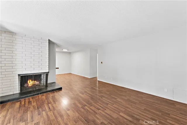 a view of an empty room with wooden floor fireplace and a window