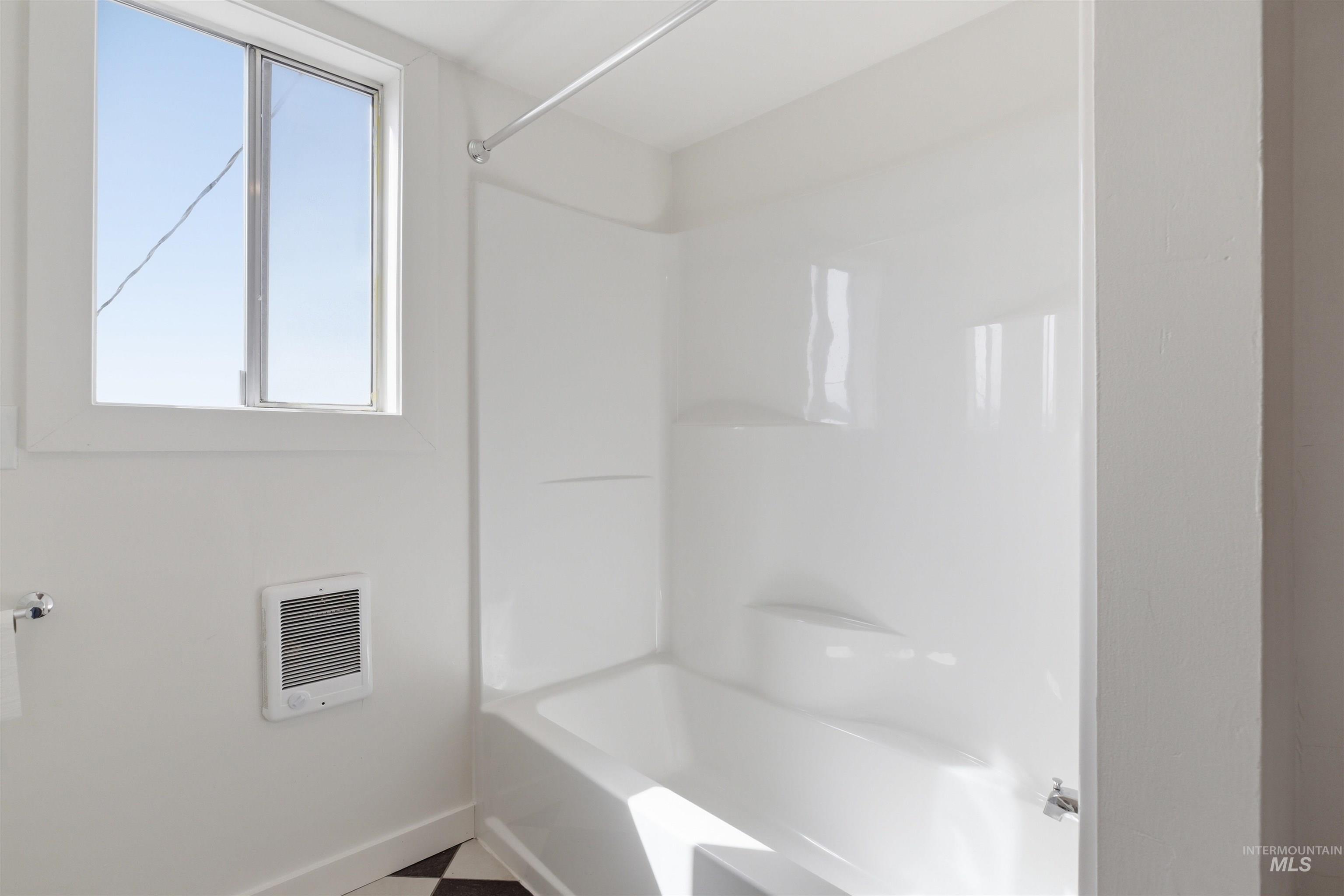 810 Pine Street Potlatch, ID 83855 - Photo 16 of 33 White acrylic tub and shower combination with a single-pane window and a wall-mounted heater