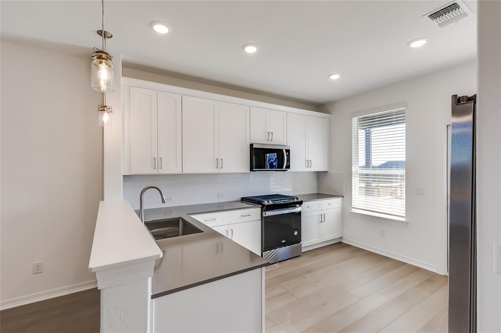 109 Bridge Deck Loop Kyle, TX 78640 - Photo 11 of 40 Kitchen featuring appliances with stainless steel finishes, white cabinets, hanging light fixtures, light wood finished floors, and backsplash