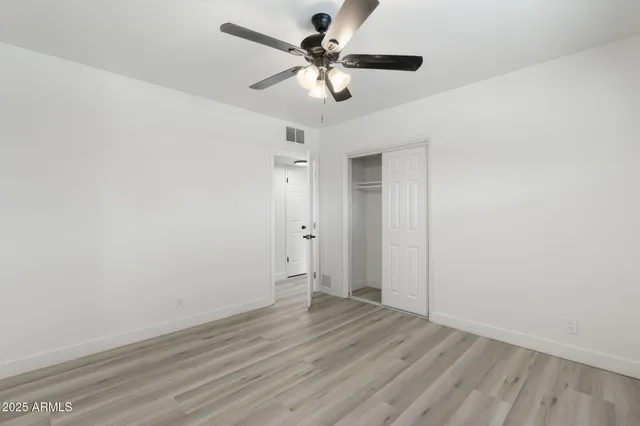 an empty room with wooden floor fan and windows