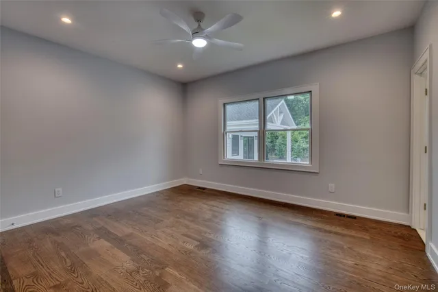 an empty room with wooden floor chandelier fan and windows