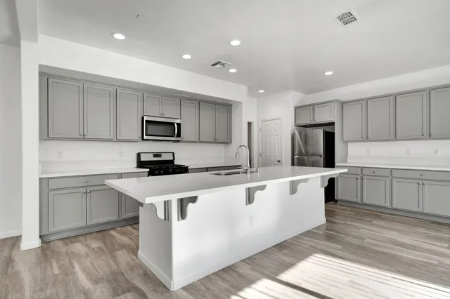 a large white kitchen with stainless steel appliances granite countertop a stove a sink a refrigerator and white cabinets with wooden floor