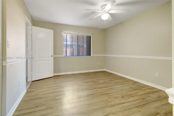 an empty room with wooden floor fan and windows