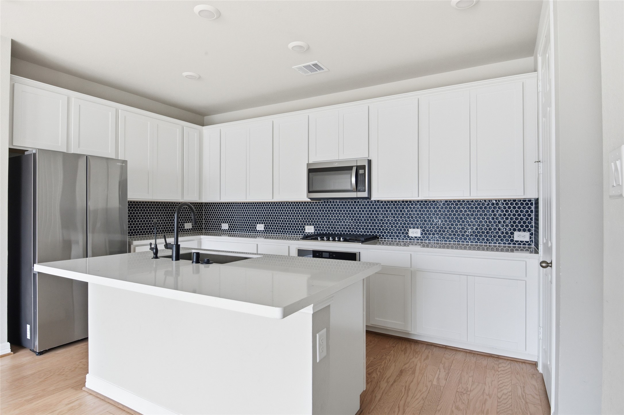 9406 Caddo Ridge Lane Cypress, TX 77433 - Photo 7 of 16 a kitchen with stainless steel appliances a sink a stove a refrigerator a white cabinets and wooden floor