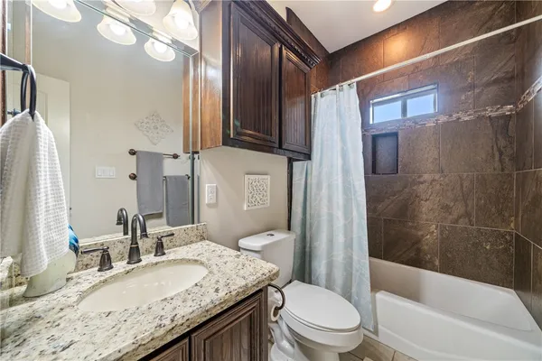 a bathroom with a granite countertop bathtub shower sink vanity mirror and toilet