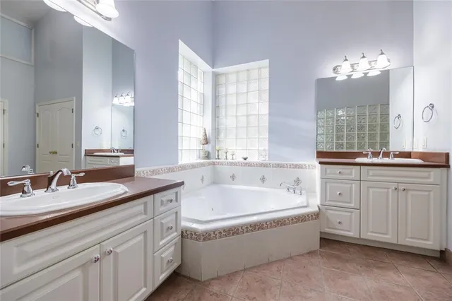 a spacious en suite bathroom with a granite countertop double vanity sink a bathtub and mirror