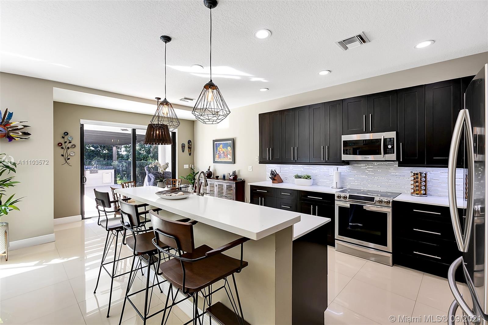 19124 Seneca Avenue Weston, FL 33332 - Photo 10 of 38 a kitchen with stainless steel appliances a stove a sink a microwave a dining table and chairs