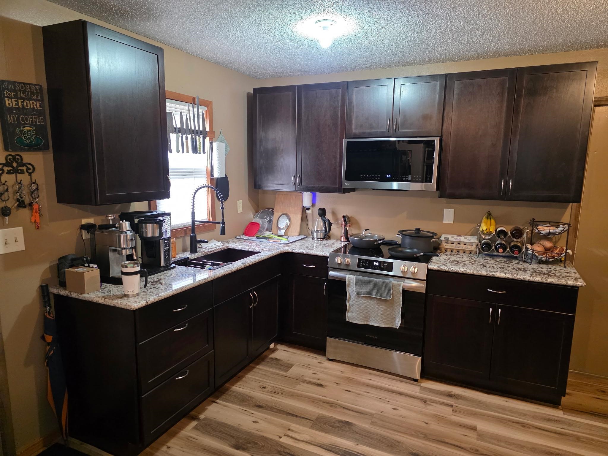 6821 Barrett Road Chisholm, MN 55719 - Photo 3 of 34 Kitchen featuring appliances with stainless steel finishes, dark brown cabinetry, a textured ceiling, light wood-style floors, and light stone countertops