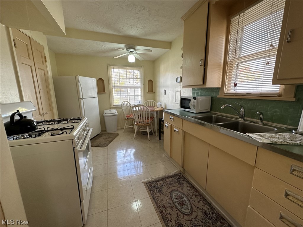 14422 Alger Road Cleveland, OH 44111 - Photo 2 of 16 Kitchen featuring light tile floors, white appliances, a textured ceiling, ceiling fan, and tasteful backsplash