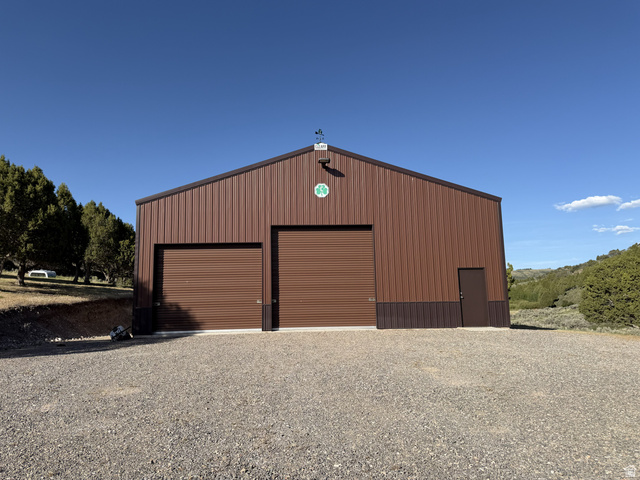 2006 Swenson Valley Road Bancroft, ID 83217 - Photo 24 of 51 Brown metal building featuring two large roll-up doors, a single entry door, and a gravel parking area