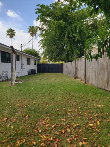 a view of a yard in front of a house with plants and large tree