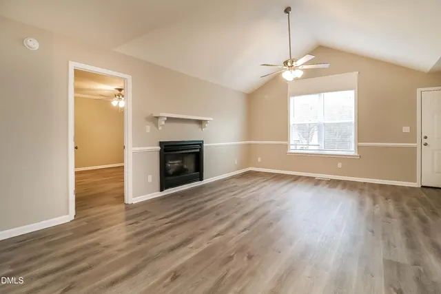 an empty room with wooden floor fireplace and windows