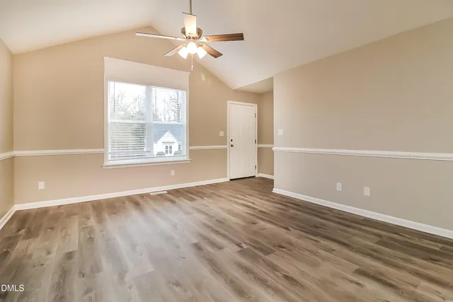 an empty room with wooden floor chandelier fan and windows