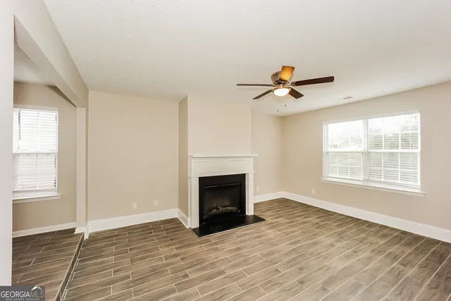 a view of an empty room with wooden floor fireplace and a window