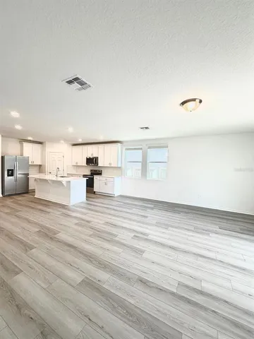a large white kitchen with stainless steel appliances kitchen island a stove a refrigerator a oven a sink dishwasher and white cabinets with wooden floor
