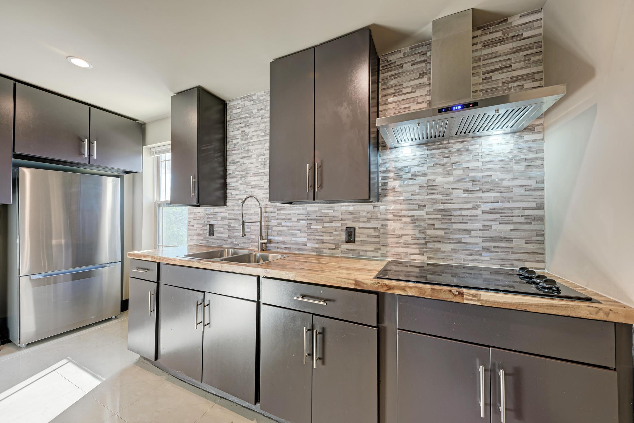 104 Spring Valley Street Hutto, TX 78634 - Photo 24 of 40 Kitchen featuring freestanding refrigerator, wall chimney exhaust hood, tasteful backsplash, butcher block counters, and black electric cooktop