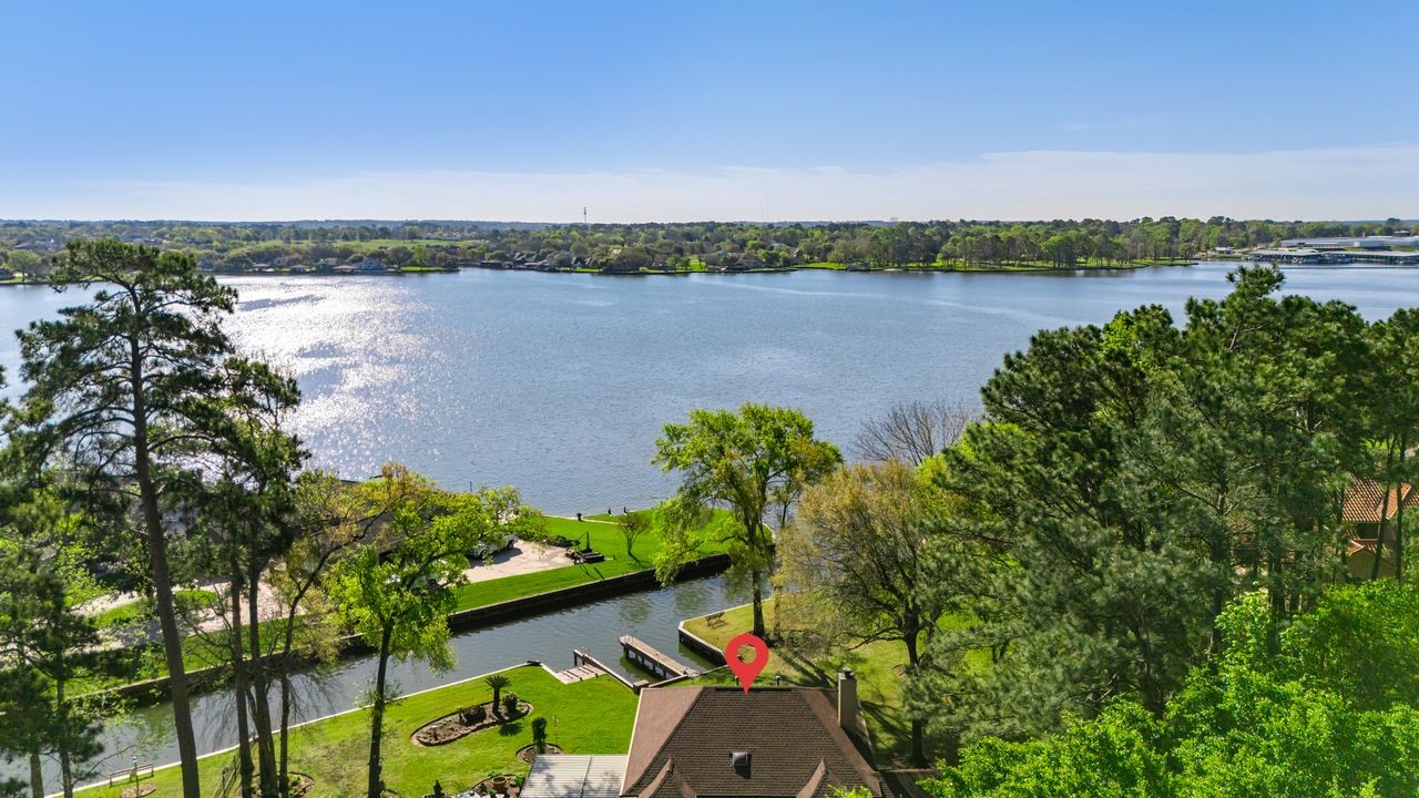 12626 Aries Loop Willis, TX 77318 - Photo 1 of 50 This photo showcases a serene lakeside property with lush greenery and mature trees, offering a picturesque view of the expansive water. Ideal for those seeking tranquility and natural beauty, the home also features a private dock, perfect for water activities and relaxation.