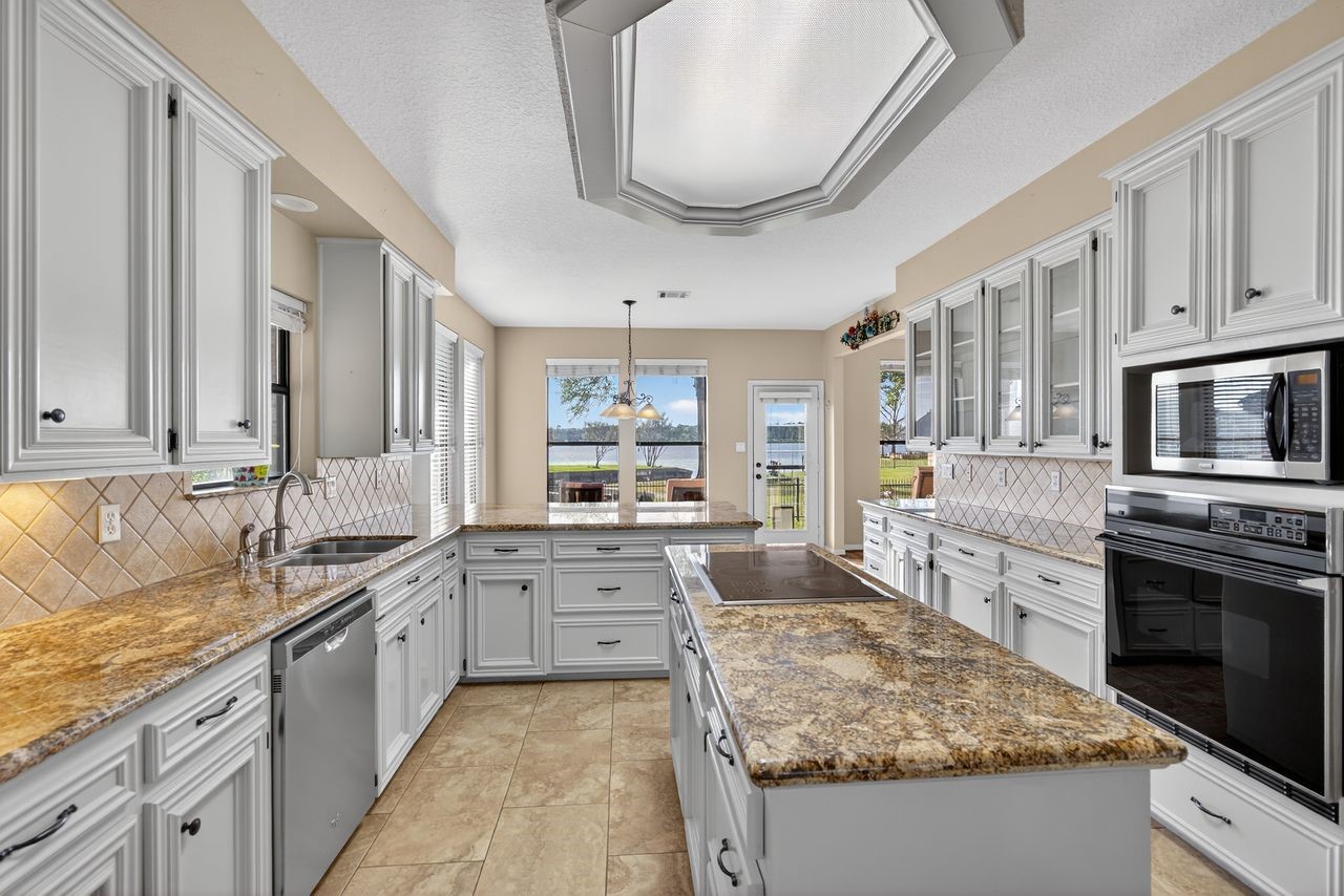 12626 Aries Loop Willis, TX 77318 - Photo 13 of 50 This kitchen features spacious granite countertops, ample white cabinetry, and stainless steel appliances. The open layout includes a large island and offers a scenic view through the windows, creating a bright and inviting space perfect for cooking and entertaining.