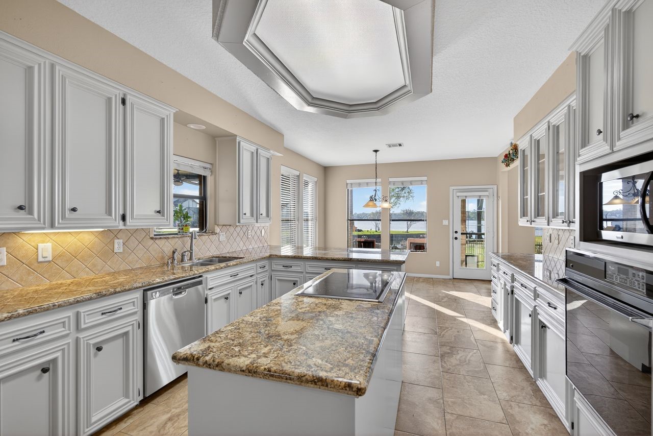 12626 Aries Loop Willis, TX 77318 - Photo 14 of 50 This spacious kitchen features elegant granite countertops, white cabinetry, and stainless steel appliances. It includes a central island with a cooktop, ample natural light, and a dining area with scenic views through large windows.