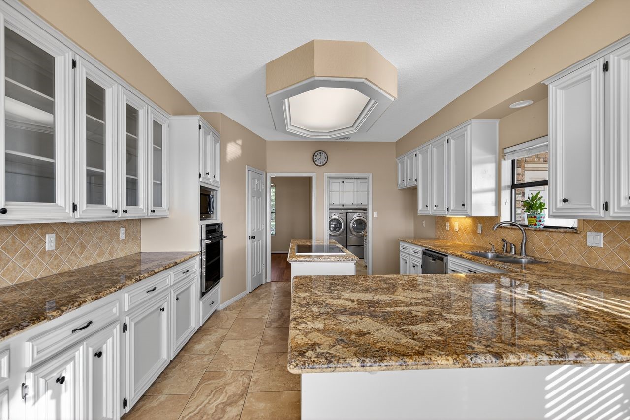12626 Aries Loop Willis, TX 77318 - Photo 15 of 50 This spacious kitchen features granite countertops, ample white cabinetry, and modern appliances, with a central island and tile flooring. It offers plenty of natural light and a view into a utility area with a washer and dryer.