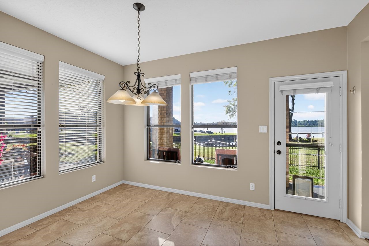 12626 Aries Loop Willis, TX 77318 - Photo 18 of 50 Bright dining area with large windows offering stunning lake views. Features tile flooring and a stylish chandelier, opening to an outdoor space through a glass door.