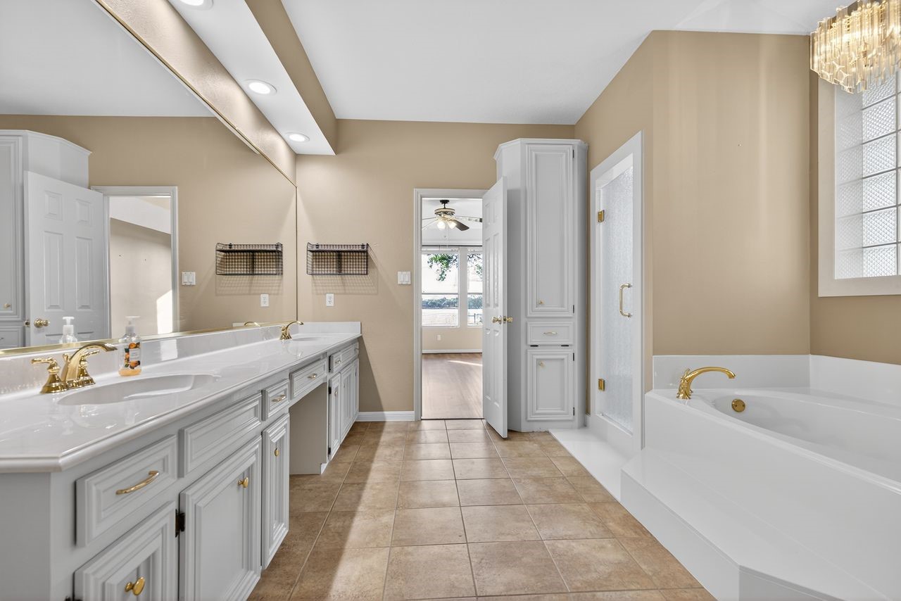 12626 Aries Loop Willis, TX 77318 - Photo 21 of 50 This spacious bathroom features a double vanity with ample storage, a luxurious soaking tub with gold fixtures, and a separate shower. The neutral color palette and large mirror enhance the sense of space and light.