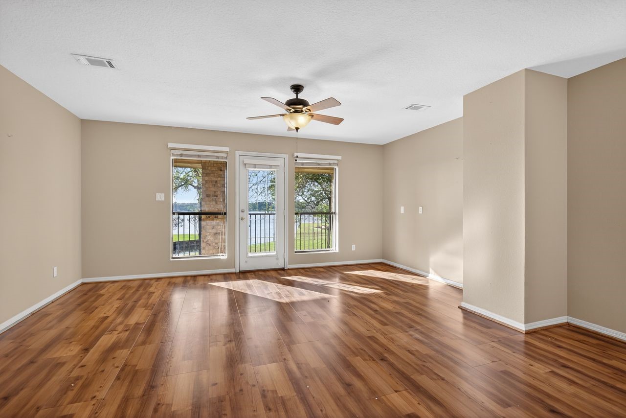 12626 Aries Loop Willis, TX 77318 - Photo 22 of 50 This spacious room features warm wood flooring and neutral walls, creating a cozy atmosphere. A ceiling fan adds comfort, while large windows and a glass door offer plenty of natural light and views of the outdoors, perfect for enjoying scenic vistas.