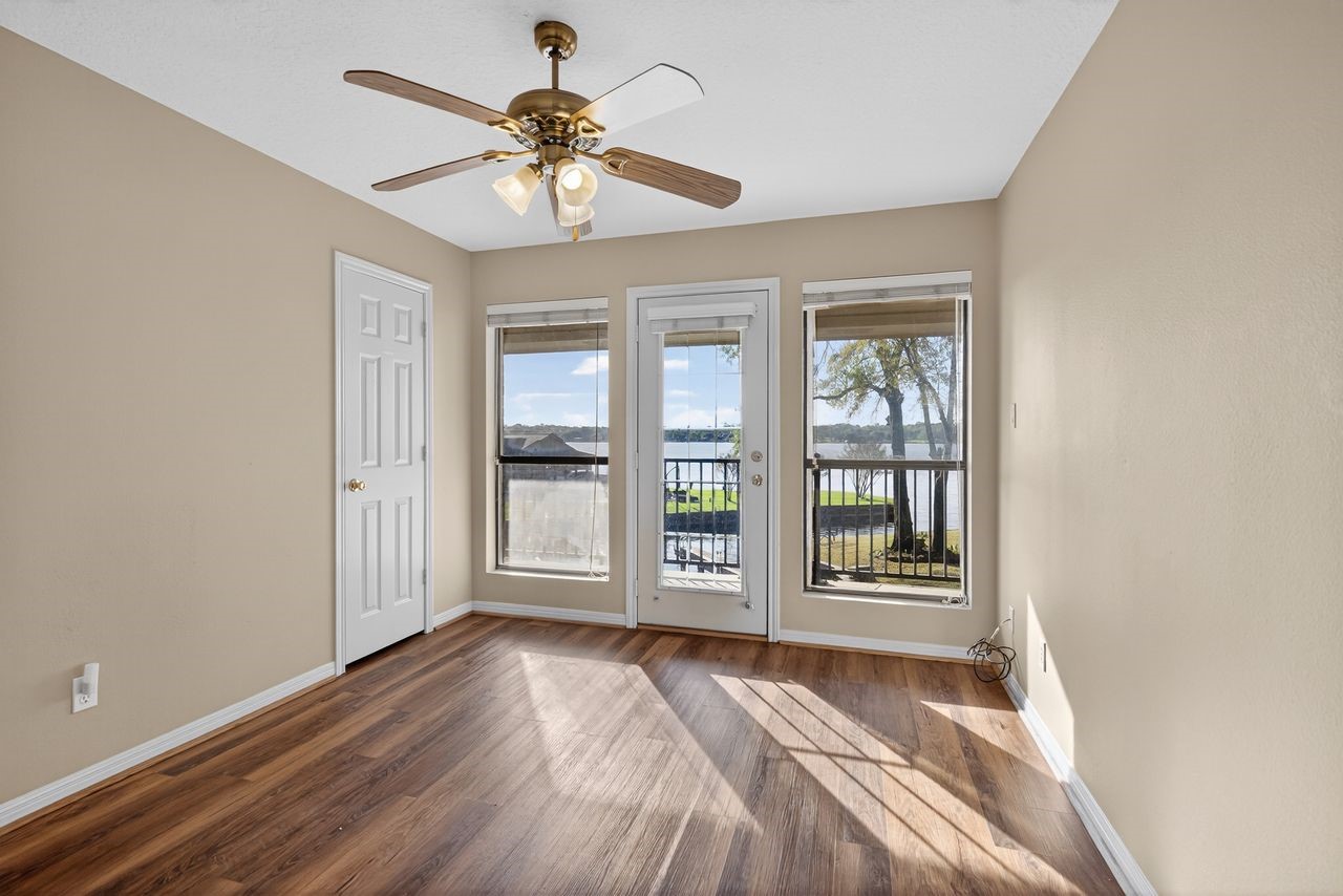 12626 Aries Loop Willis, TX 77318 - Photo 26 of 50 This bright room features hardwood floors, a ceiling fan, and large windows with a door leading to a balcony, offering a scenic view of the water and surrounding landscape.