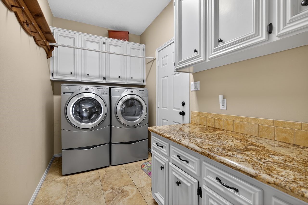 12626 Aries Loop Willis, TX 77318 - Photo 27 of 50 This photo showcases a well-organized laundry room with modern appliances, ample cabinetry for storage, and a spacious countertop with a granite finish. The neutral color scheme and tile flooring add a clean, functional feel to the space.