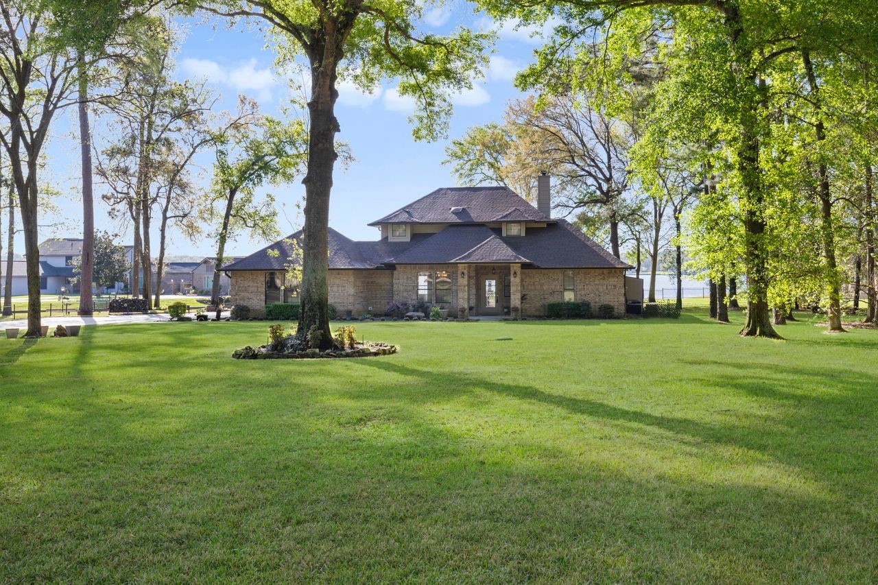 12626 Aries Loop Willis, TX 77318 - Photo 31 of 50 A charming brick house set on a spacious, lush lawn surrounded by mature trees, offering privacy and a serene atmosphere.