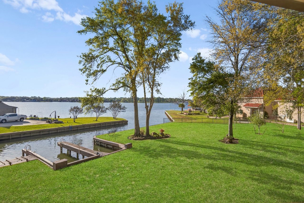 12626 Aries Loop Willis, TX 77318 - Photo 33 of 50 This photo showcases a serene waterfront property with a well-maintained green lawn, mature trees, and a private dock. Perfect for enjoying peaceful lake views and outdoor activities.