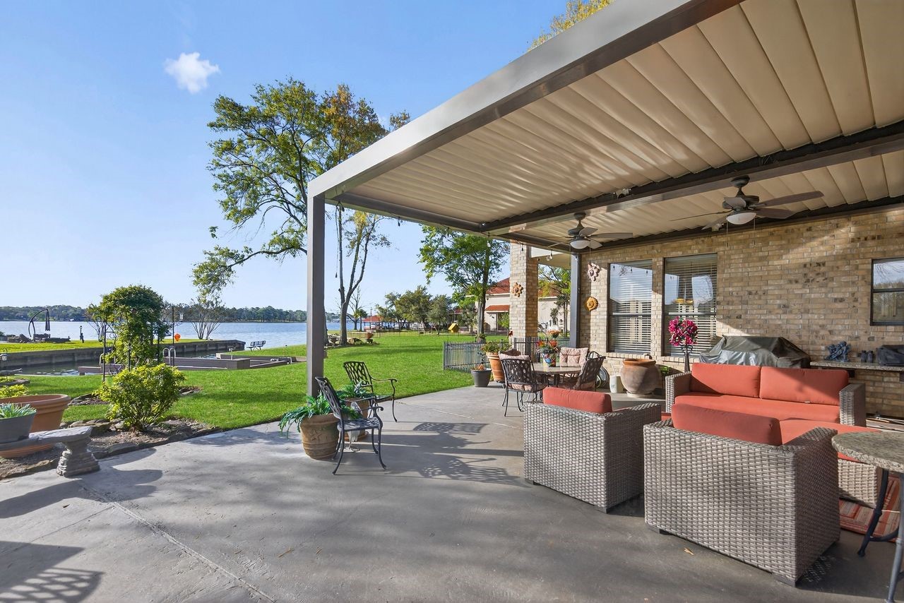 12626 Aries Loop Willis, TX 77318 - Photo 34 of 50 This photo showcases a spacious patio with a stylish pergola, comfortable outdoor seating, and a beautiful view of a lakeside setting. Ideal for relaxation and entertaining, the area offers lush greenery and waterfront access.