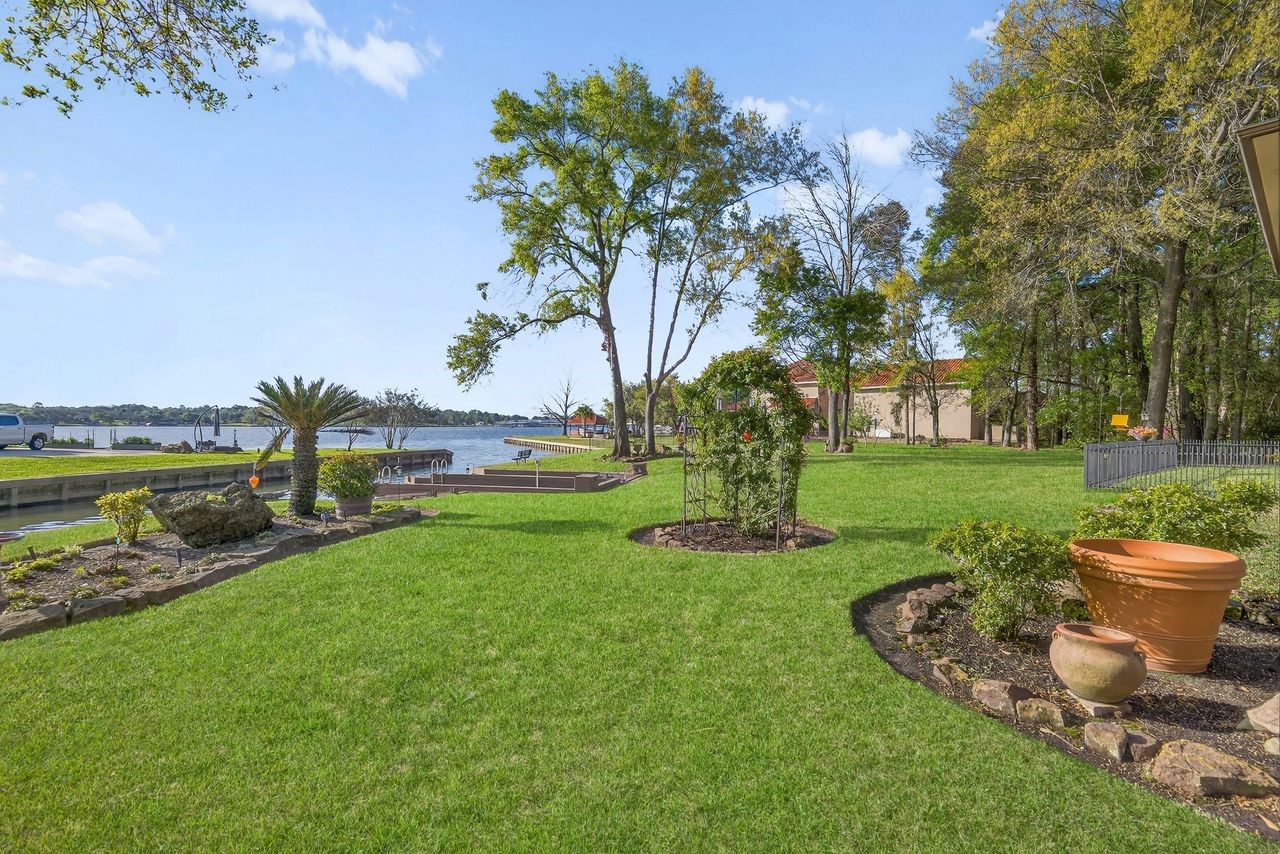 12626 Aries Loop Willis, TX 77318 - Photo 37 of 50 This photo showcases a spacious, well-maintained backyard with lush green grass and landscaped garden beds. It features a scenic waterfront view, complete with a dock, providing an ideal setting for outdoor relaxation and recreation.