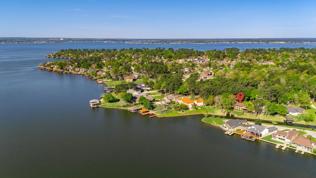 12626 Aries Loop Willis, TX 77318 - Photo 39 of 50 This aerial photo showcases a picturesque lakeside community with lush greenery and a variety of homes along the water's edge. The highlighted property offers scenic views and direct waterfront access, perfect for those seeking a serene, nature-filled living environment.