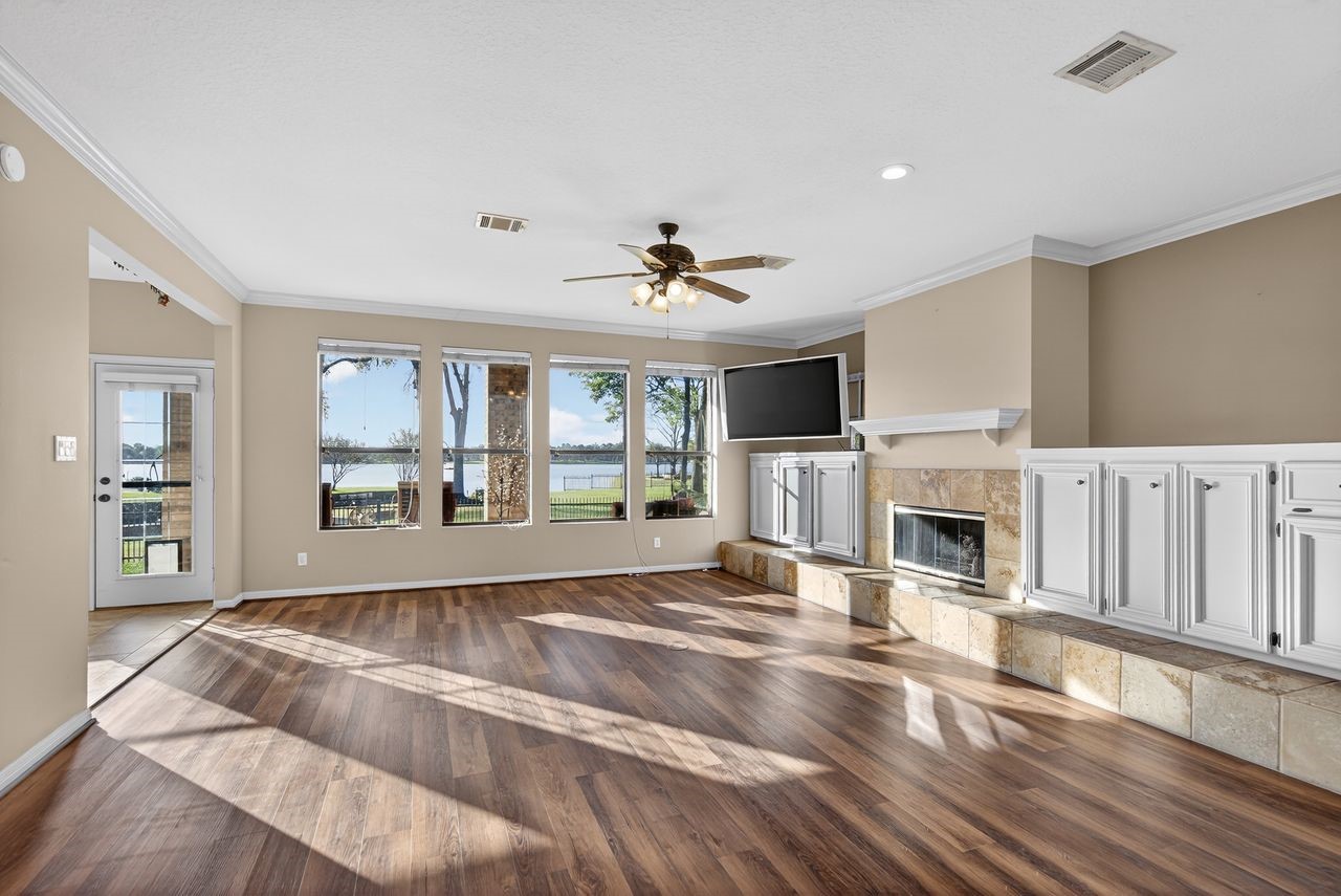 12626 Aries Loop Willis, TX 77318 - Photo 4 of 50 This spacious living room features large windows with a beautiful water view, hardwood floors, a ceiling fan, a fireplace, and built-in cabinetry. Ideal for comfortable living and entertaining.