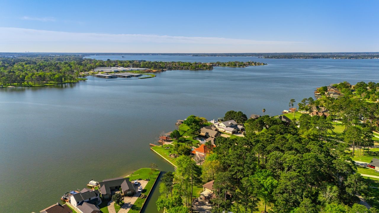 12626 Aries Loop Willis, TX 77318 - Photo 41 of 50 This photo showcases a serene lakeside neighborhood with lush greenery and waterfront homes. The expansive lake offers scenic views and recreational opportunities, ideal for those seeking a tranquil and picturesque living environment.
