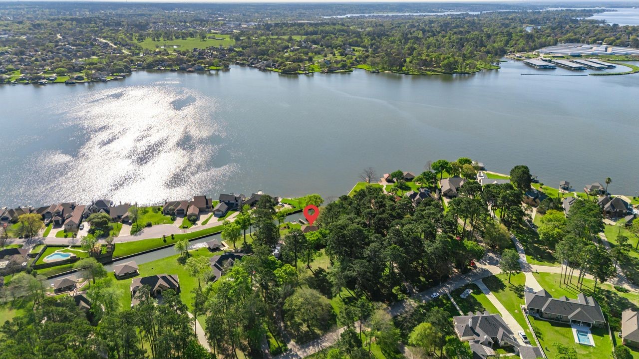 12626 Aries Loop Willis, TX 77318 - Photo 45 of 50 This aerial photo showcases a picturesque lakeside neighborhood with spacious homes surrounded by lush greenery. The area offers serene water views and ample privacy, ideal for those seeking a tranquil living environment.
