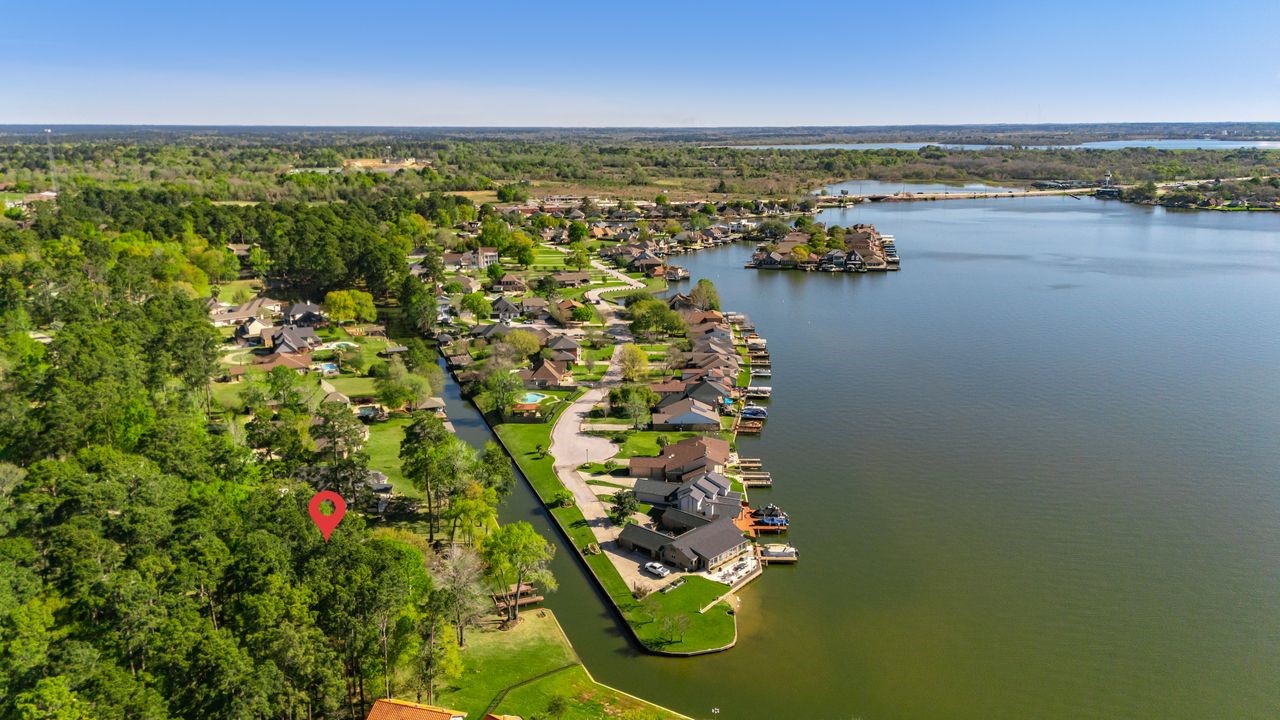 12626 Aries Loop Willis, TX 77318 - Photo 47 of 50 This aerial photo showcases a picturesque lakeside community, featuring waterfront homes with docks, lush greenery, and a serene waterway. A highlighted point indicates a specific property nestled among trees, offering a blend of nature and lakeside living.