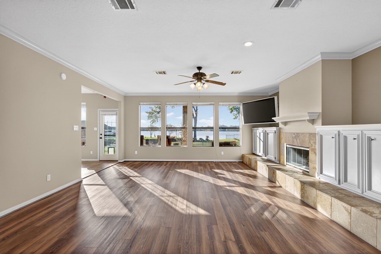 12626 Aries Loop Willis, TX 77318 - Photo 5 of 50 This spacious living room features large windows with scenic lake views, abundant natural light, a cozy fireplace, and elegant wood flooring.