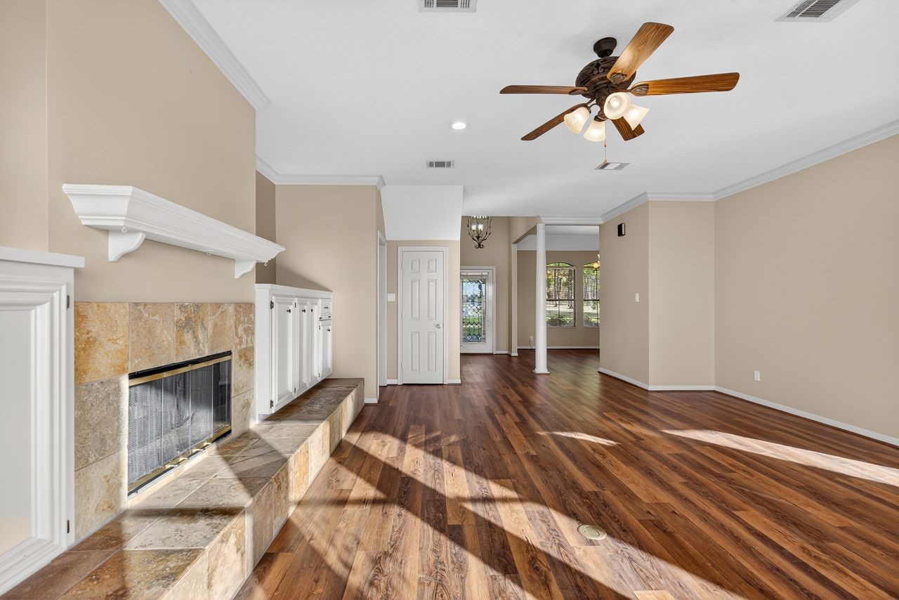 12626 Aries Loop Willis, TX 77318 - Photo 6 of 50 This spacious living area features warm wood flooring, a cozy stone fireplace, and a ceiling fan. The neutral walls and ample natural light create an inviting atmosphere, perfect for relaxation.