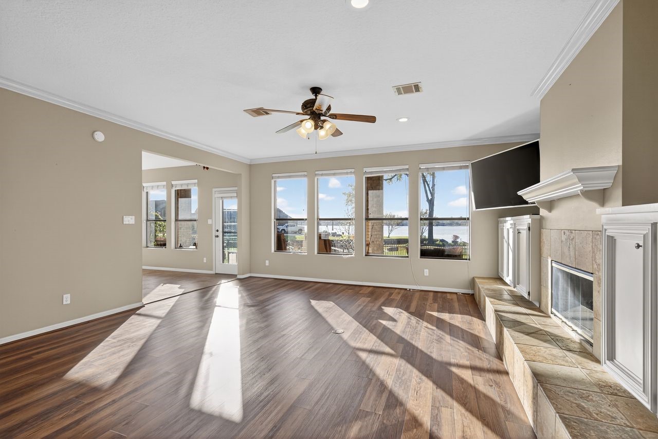 12626 Aries Loop Willis, TX 77318 - Photo 7 of 50 This spacious living room features large windows with scenic views, a cozy fireplace, and wood flooring. The open layout is enhanced by a ceiling fan and neutral tones, perfect for natural light and comfort.